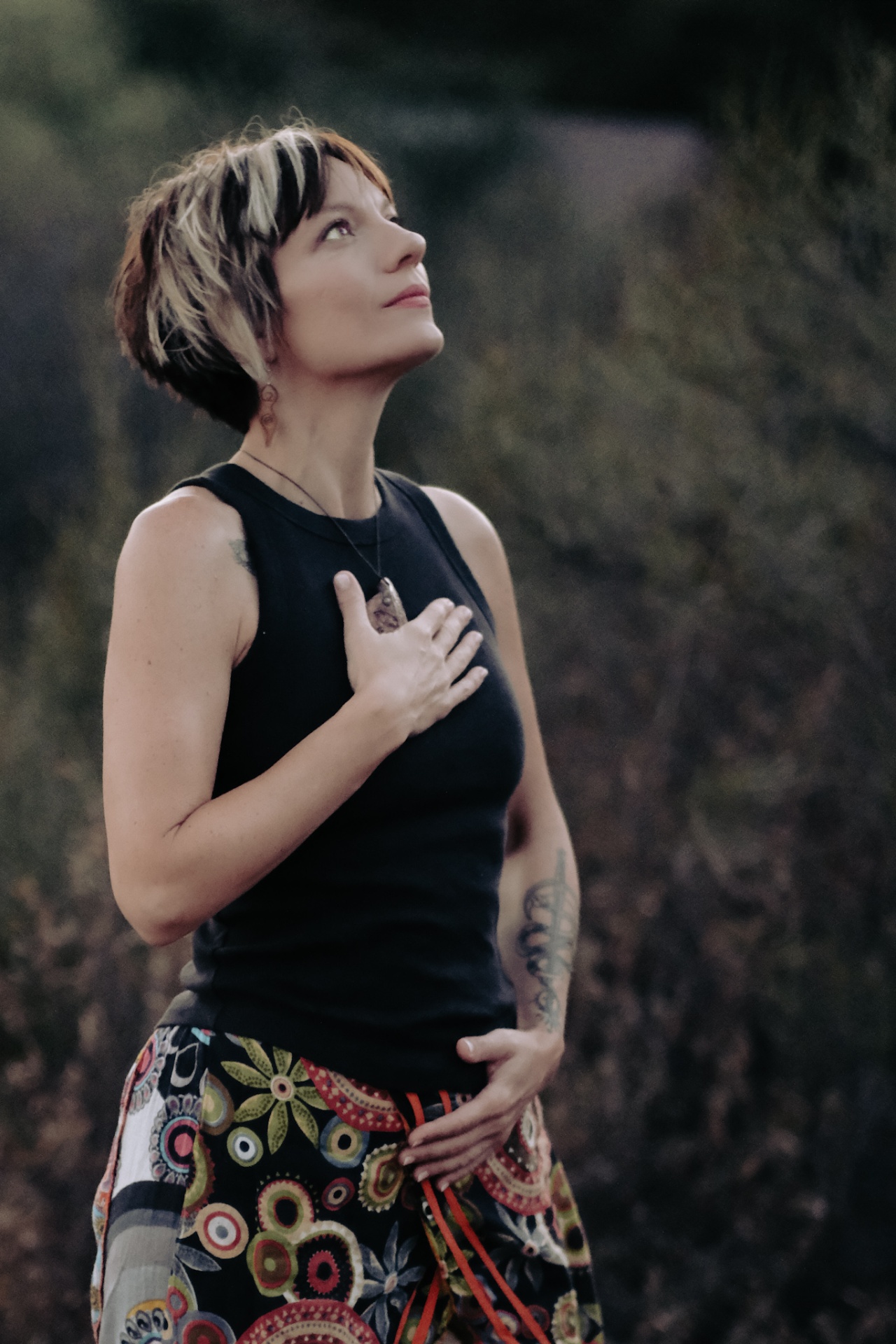 Janelle, founder of Bee Well with Janelle, standing outdoors with her hand on her heart